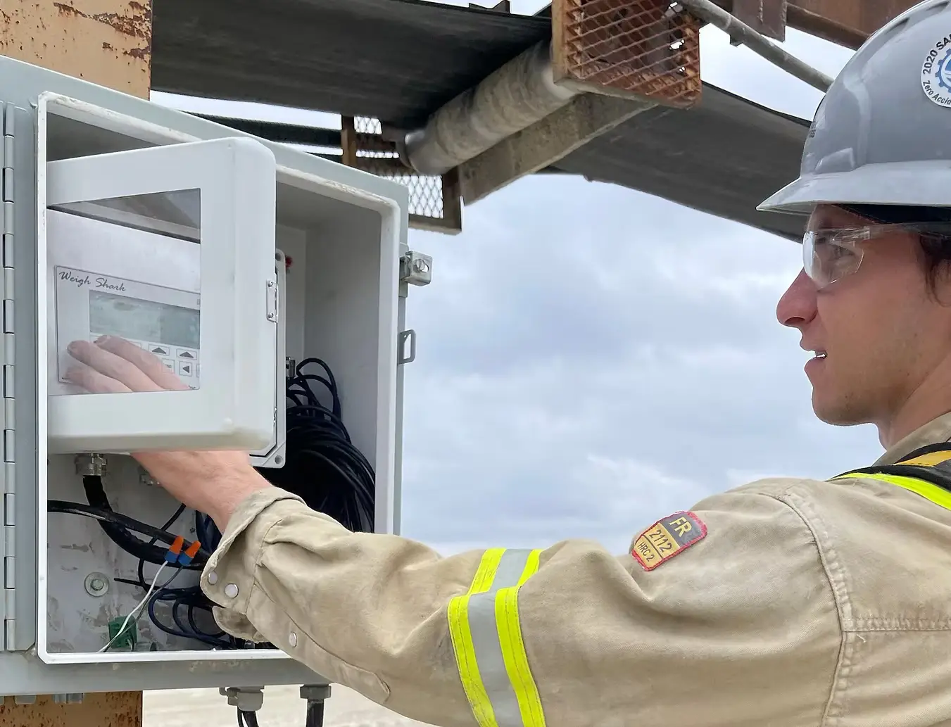 Technician Inspecting Electrical Control Panel in Industrial Site Industrial technician inspecting and adjusting an electrical control box outdoors, wearing PPE including a hard hat and safety glasses