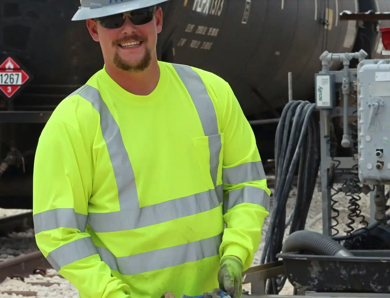 Worker Wearing High-Visibility Safety Gear Operating Industrial Equipment Male worker in high-visibility reflective safety clothing operating industrial equipment near a fuel container labeled 1267